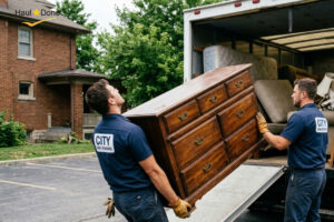 Two workers in uniform lifting a large wooden dresser into the back of a junk removal truck